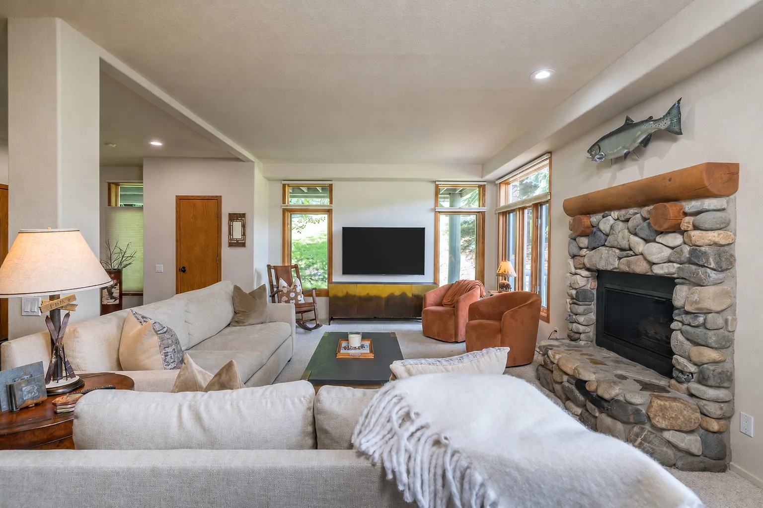 A bright living room with cream sofas and a river-rock fireplace.
