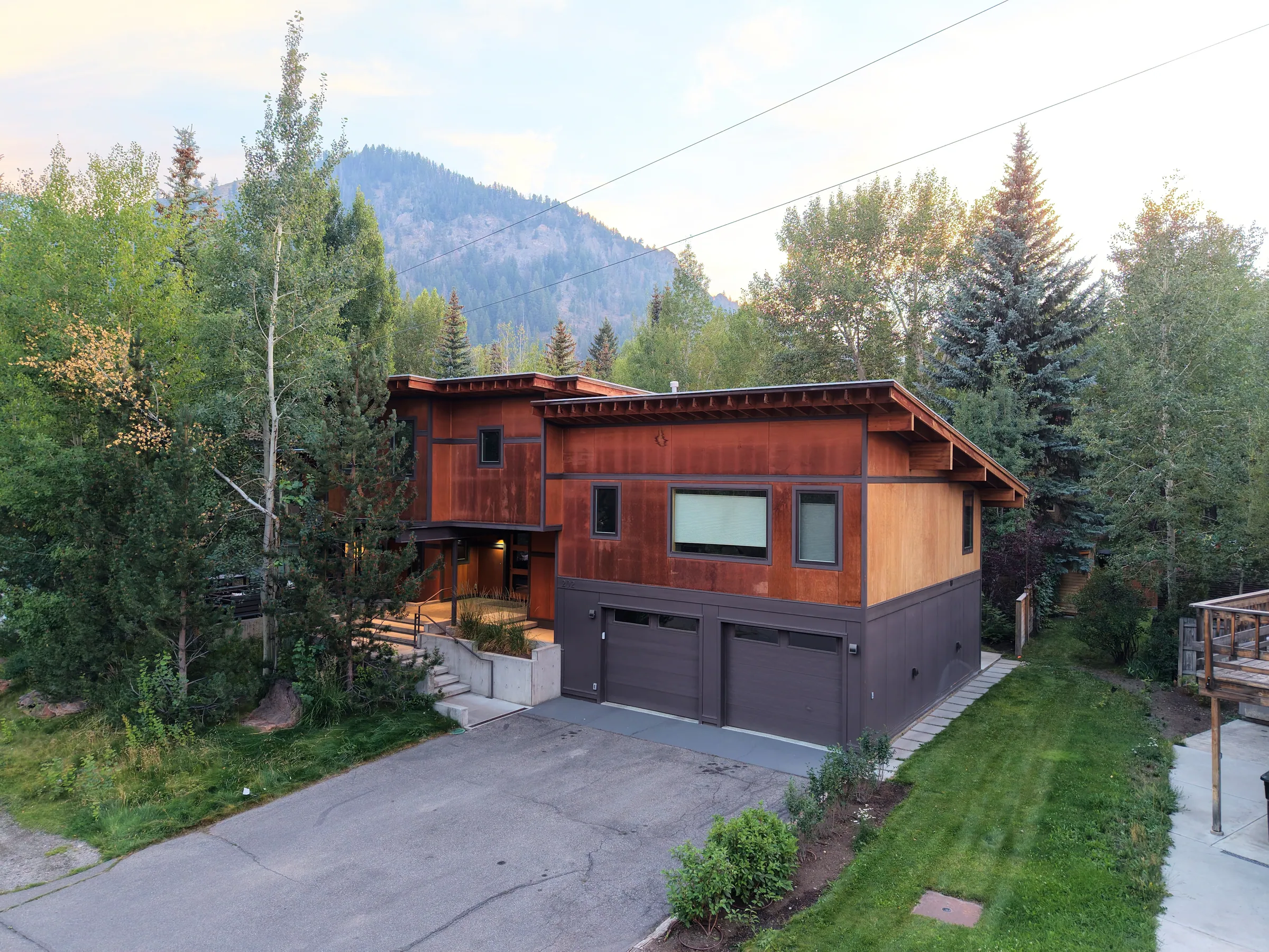 A contemporary home with rust-colored siding surrounded by trees and mountains.