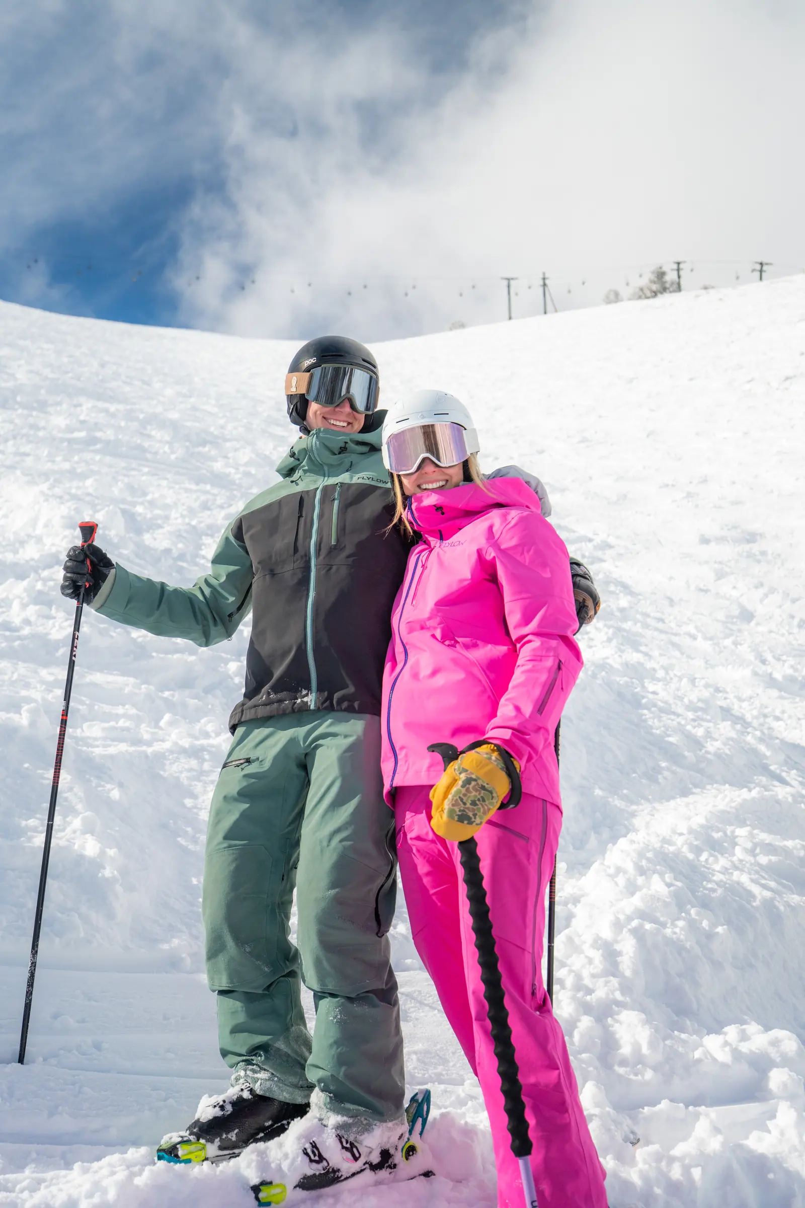 Two skiers together on a snowy slope beneath a blue and cloudy sky.